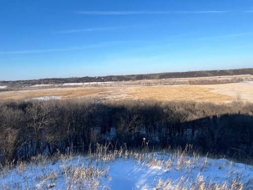 A scenic view of a snowy landscape with fields and trees under a clear blue sky.
