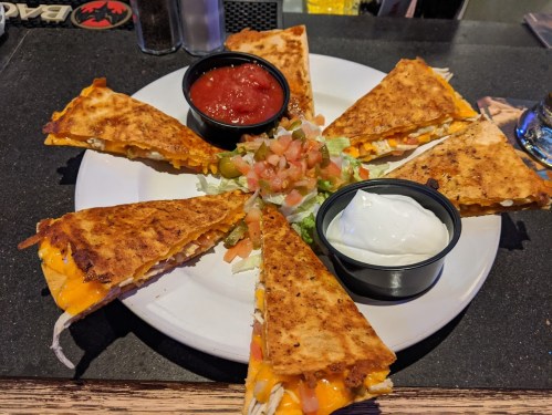 A plate of quesadillas arranged in a circle, served with salsa, sour cream, and a fresh pico de gallo salad.