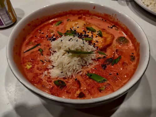 A bowl of creamy red curry with rice, topped with green onions and black sesame seeds.
