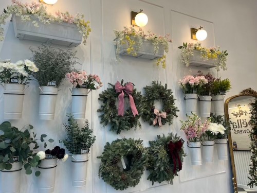A wall display featuring floral arrangements and wreaths in white containers, adorned with soft pastel colors and greenery.
