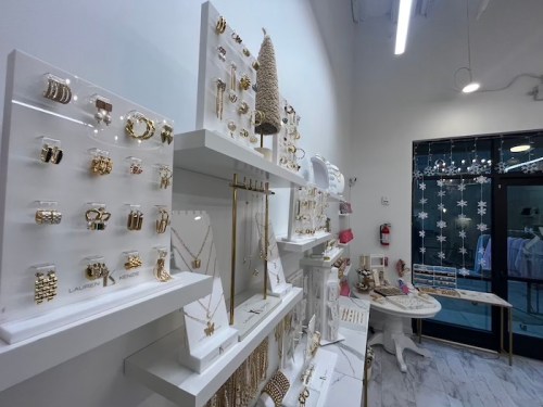A display of gold jewelry on white shelves in a bright store, with festive decorations in the background.