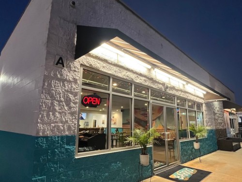 A brightly lit restaurant exterior at night, featuring an "OPEN" sign and decorative plants by the entrance.