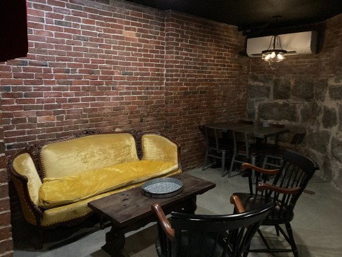 Cozy room with exposed brick walls, featuring a yellow sofa, wooden table, and black chairs.