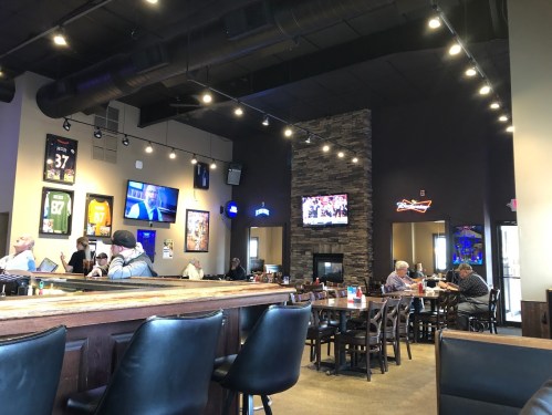 Interior of a sports bar with tables, a bar area, TVs showing games, and patrons enjoying their time.