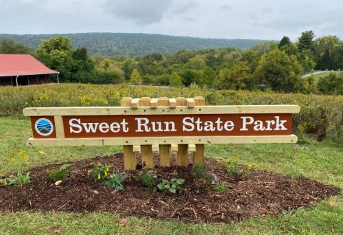 Sign for Sweet Run State Park, surrounded by greenery and hills in the background.