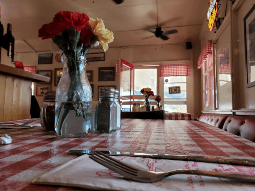A cozy restaurant table with a checkered tablecloth, a vase of flowers, and utensils ready for dining.
