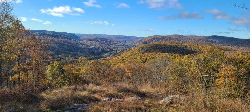 A scenic view of rolling hills covered in autumn foliage under a blue sky with fluffy clouds.