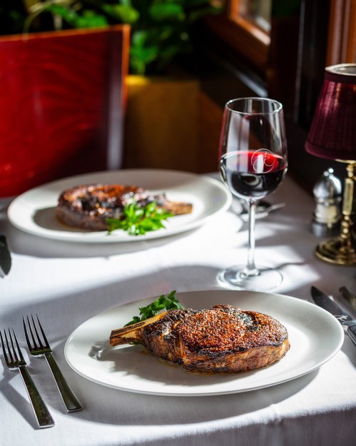 A beautifully plated ribeye steak with a glass of red wine on a white tablecloth, set in an elegant dining setting.