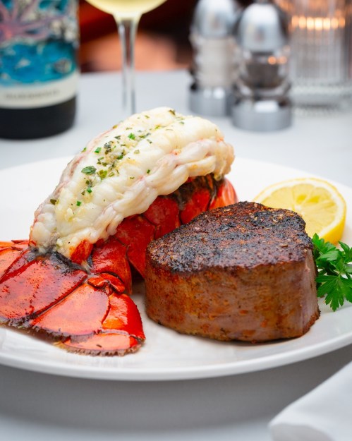 A plate featuring a grilled lobster tail and a seared filet mignon, garnished with lemon and parsley.