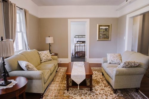 Cozy living room with two sofas, a coffee table, and a view of a bedroom through an open doorway.