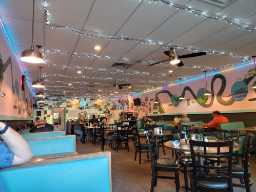 Cozy diner interior with string lights, colorful wall decor, and patrons enjoying meals at tables.