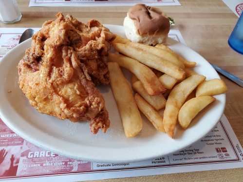 A plate of fried chicken, golden fries, and a soft bun on a table with a menu in the background.