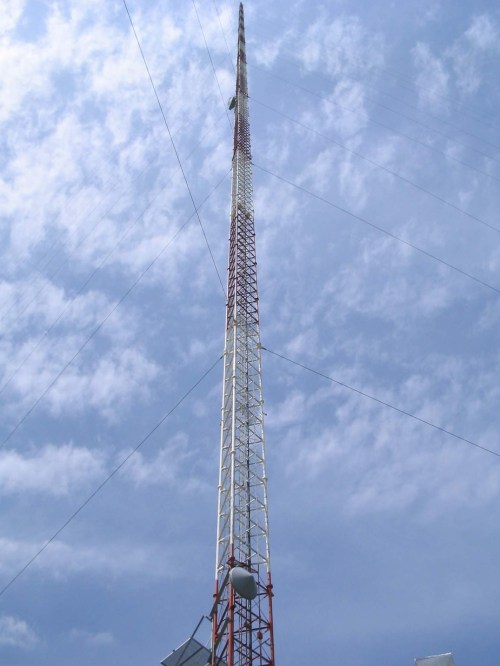 A tall communication tower reaching into a blue sky with scattered clouds.