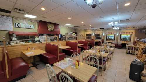 A cozy diner interior with red booths, tables, and a kitchen area, featuring condiments on tables and warm lighting.