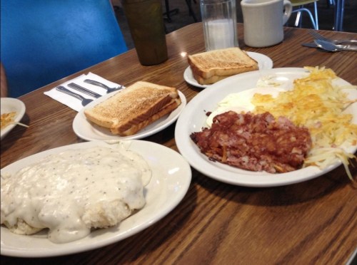 A table setting with toast, a plate of biscuits and gravy, hash browns, and crispy bacon.