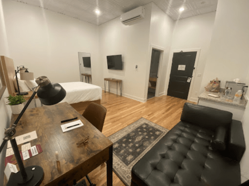Cozy hotel room featuring a bed, desk, TV, seating area, and modern decor with wooden floors.