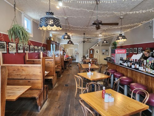 Cozy restaurant interior with wooden booths, tables, and a bar, adorned with string lights and vintage decor.