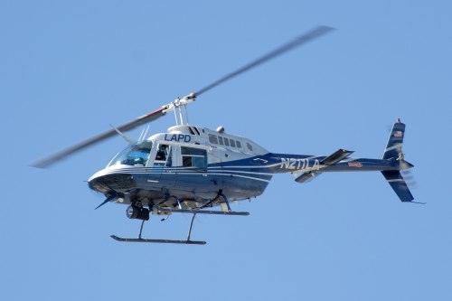 A blue and white LAPD helicopter flying against a clear blue sky.