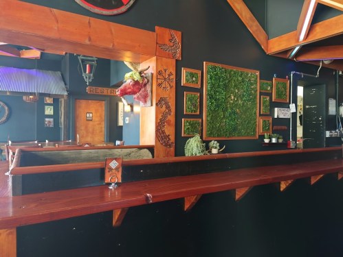 Interior of a restaurant featuring wooden accents, green wall art, and a bar area with a mirror reflecting the space.
