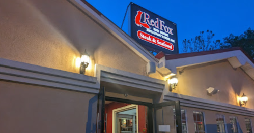 Exterior of Red Fox Steak & Seafood restaurant at dusk, featuring a lit sign and welcoming entrance.