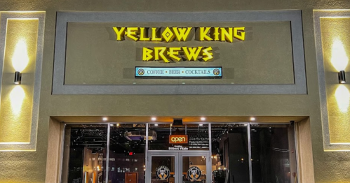 Sign for "Yellow King Brews" featuring coffee, beer, and cocktails, with an illuminated open sign at the entrance.