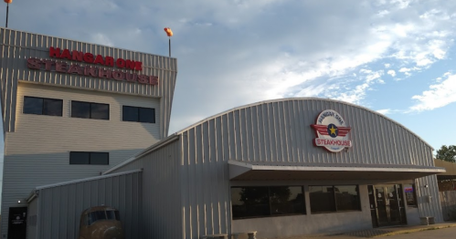Exterior of Hangar One Steakhouse, featuring a modern building with a curved roof and a vintage vehicle in front.
