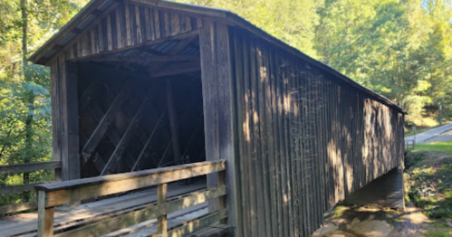 A rustic wooden covered bridge surrounded by lush greenery and trees.