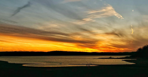 A serene sunset over a calm lake, with vibrant orange and yellow hues blending into the sky.