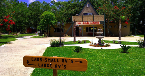 A sign points to parking areas for small and large RVs in front of a campground building surrounded by greenery.