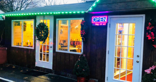 A cozy wooden building with festive decorations, illuminated "OPEN" sign, and wreaths on the doors.