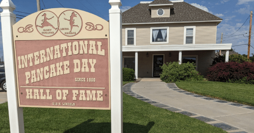 Sign for International Pancake Day Hall of Fame in Liberal, Kansas, with a house in the background.