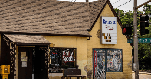 A quaint café with a yellow exterior, featuring a sign for daily specials and a colorful mural on the side.