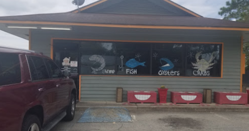 A seafood restaurant with a colorful sign displaying shrimp, fish, oysters, and crabs, parked car in front.