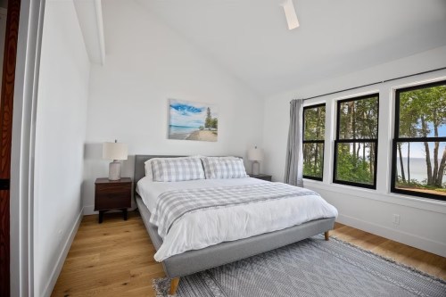 Bright, modern bedroom with a large bed, two lamps, and windows overlooking a scenic view of trees and water.
