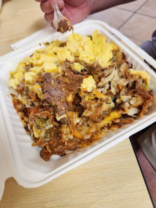 A close-up of a takeout container filled with scrambled eggs, cheese, hash browns, and beef. A fork is being used to serve.