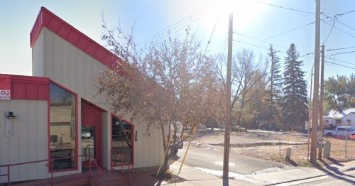 A modern building with a red roof and large windows, surrounded by trees and power lines on a sunny day.