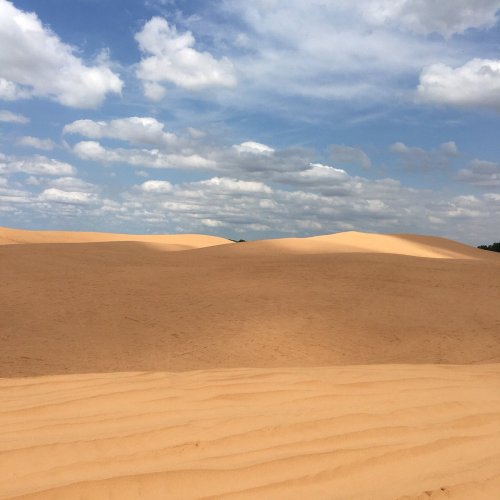 A vast desert landscape with rolling sand dunes under a partly cloudy sky.