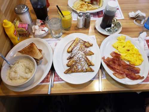 A breakfast spread featuring French toast, scrambled eggs, bacon, grits, toast, and drinks on a wooden table.