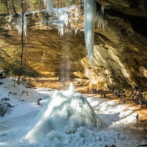 A snowy landscape with ice formations and people exploring a cave-like area surrounded by towering cliffs.