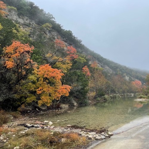 A serene river scene surrounded by colorful autumn trees and misty mountains in the background.
