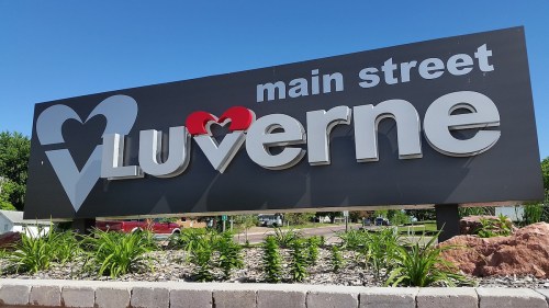 Sign for Main Street Luverne featuring a heart design, surrounded by greenery and a clear blue sky.