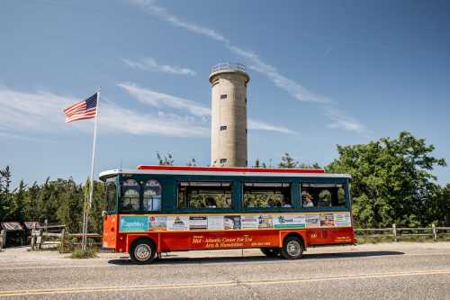 A colorful tour bus parked near a tall tower, with an American flag waving in the background and trees nearby.