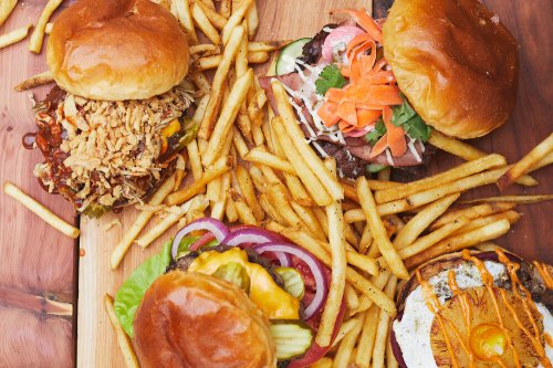 A variety of gourmet burgers topped with fresh ingredients, served with a side of crispy fries on a wooden platter.