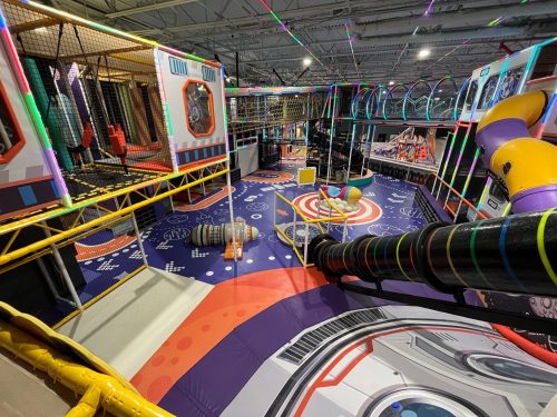A colorful indoor play area with slides, climbing structures, and a space-themed design.