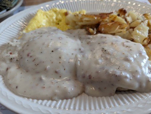 A plate of biscuits and gravy, scrambled eggs, and crispy hash browns.