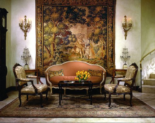 Elegant sitting area featuring a tapestry, ornate chairs, a floral centerpiece, and soft lighting.