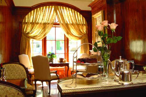 Elegant room with wooden accents, a window draped in gold curtains, and a tea set with roses on a table.