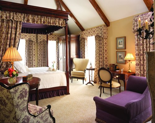 Elegant bedroom with a four-poster bed, floral curtains, and classic furniture, featuring warm lighting and a cozy atmosphere.