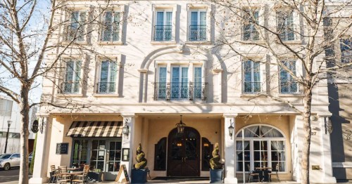 A charming building with large windows, balconies, and outdoor seating, surrounded by bare trees on a sunny day.