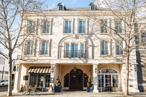A charming building with a light-colored facade, large windows, and outdoor seating under bare trees.